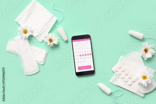 Menstrual calendar on screen of mobile phone and feminine hygiene products on...