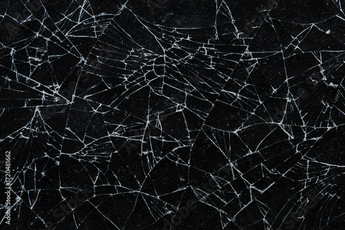 Broken glass texture with intricate crack patterns on a black background. The detailed shards and broken lines form a dramatic abstract motif, suitable for concepts of damage, destruction, and shards.