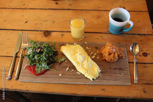 farm to table breakfast setting of omelette, greens, tomato, and butternut squash on a wooden plate with a small orange juice and coffee