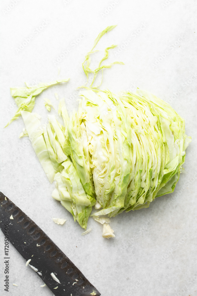 Obraz premium Overhead view of sliced cabbage on a marble countertop, top view of cabbage leaves being shredded, green cabbage being sliced