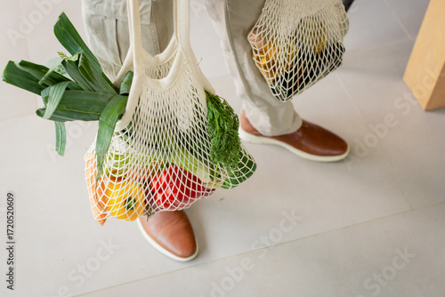 African American man standing on gray tile floor holding off-white mesh bags filled with produce