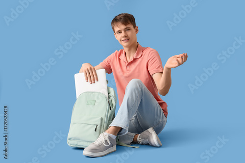 Male student taking laptop from backpack on blue background