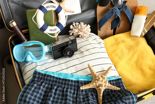 Sticker Open suitcase with men's swimwear and beach accessories on sofa, closeup