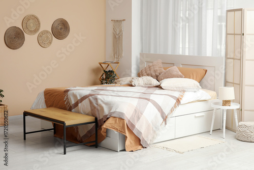 Big comfortable bed and bench near beige wall in interior of bedroom