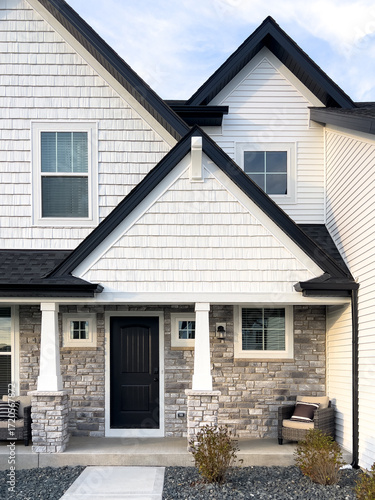 A front door detail with white composite siding, white pillars on a covered front porch, and rock siding accent. 