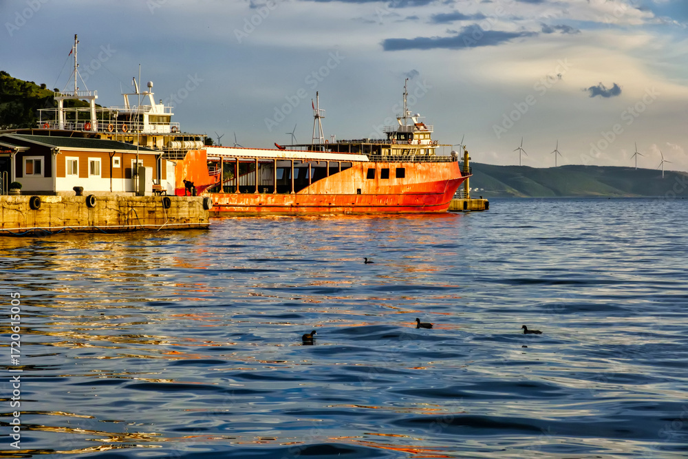 Fototapeta premium Erdek, Turkey - February 8, 2024 : Erdek Town harbor with ships at sunset