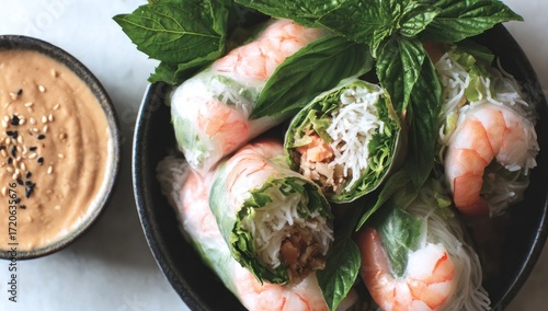 Fresh shrimp spring rolls arranged in a dark bowl, alongside a light brown peanut sauce, offer a flavorful and healthy dish.