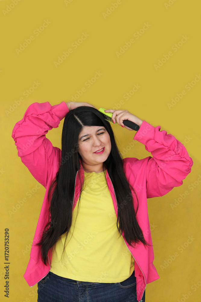 Fototapeta premium 30-year-old Latina woman brushes her long, straight hair, suffering from damaged, dehydrated, and tangled hair