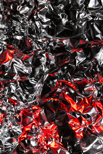 Shiny crumpled foil with silver and red reflections creating a metallic abstract design. Futuristic texture with chrome surface and cyberpunk background style