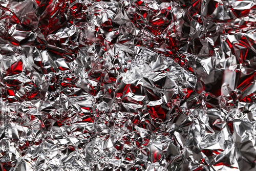 Close-up of crumpled metallic foil with shiny silver and red reflections, creating an abstract futuristic texture