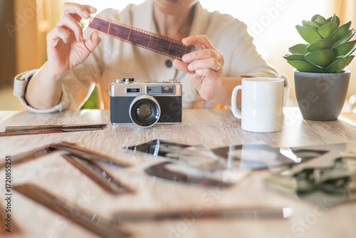Vászonkép Woman holding a strip of developed film near an old vintage camera on a wooden t