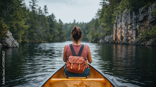 In Canadian Algonquin Park in summer, a woman in a pink top sits on the bow of an orange canoe with blue stripes and rows towards the camera
