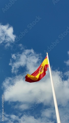 The national flag of spain fluttering on a flagpole against a beautiful blue sky with clouds