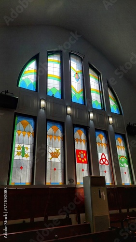 This is a detailed photo of a large, multi-paneled stained-glass window inside a church or chapel. 