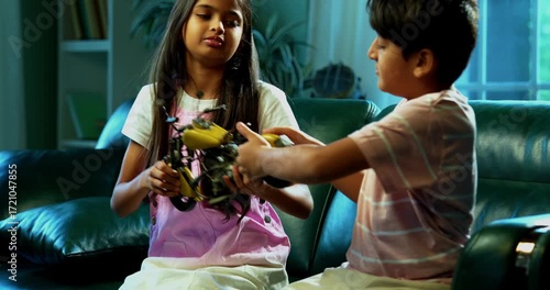 Indian Asian small sibling kids fighting over toy bike while sitting on sofa in modern home interior, one child upset while brother and sister argue, family bonding, sibling rivalry