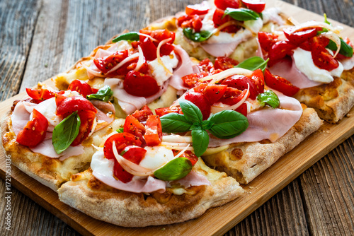 Pinsa Romana with boiled ham, cherry tomatoes, burrata cheese and basil leaves on wooden table	