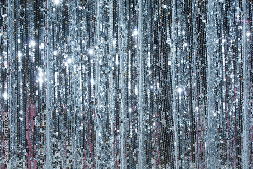 Shimmering silver curtain made of sequins glistening under bright lights in an indoor event space during the evening