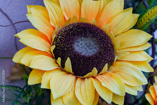 Bright artificial sunflower close-up on a wall, showcasing vibrant yellow petals and dark center