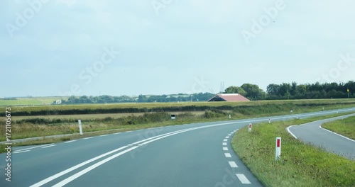 Cinematic 4K footage showing a driver’s perspective on a winding countryside road in Texel Netherlands with a large flock of birds flying across the sky over open fields