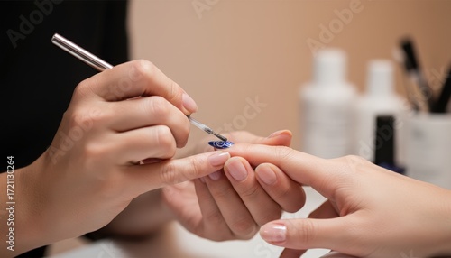 Close-up of a manicurist applying blue nail polish with a brush to a client's fingernail in a beauty salon.