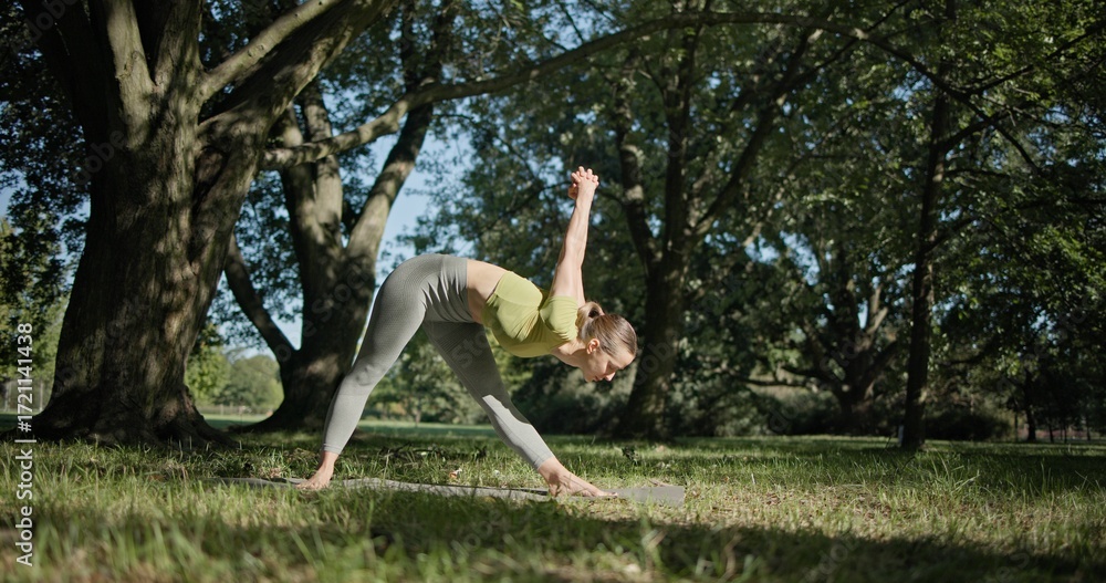 Fototapeta premium young beautiful white girl doing yoga in park among trees in clearing on summer day