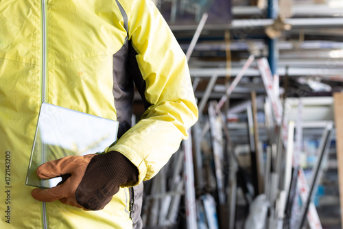 A glazier stands wearing gloves holding thick glass in a glass factory.