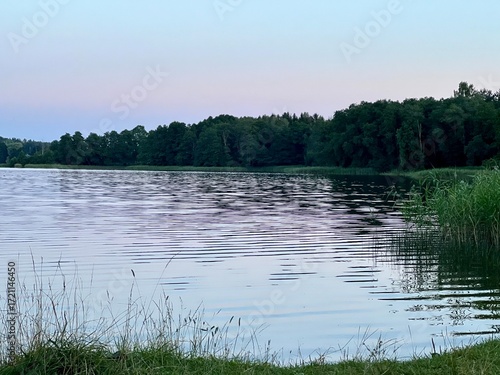 фотографія A tranquil rural lake at sunset, reflecting the soft hues of the evening sky