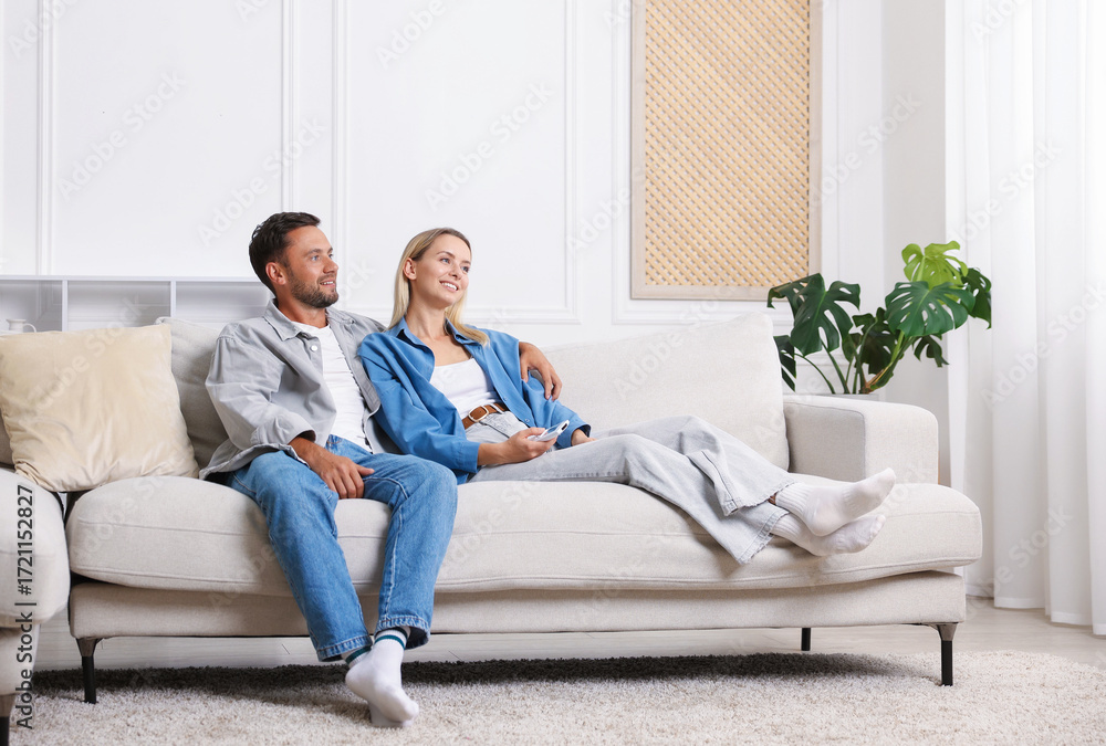 Fototapeta premium Couple with air conditioner remote control on sofa at home