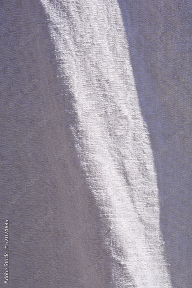 The textured surface of a linen sheet with a diagonal shadow, highlighting the folds and wrinkles in the fabric