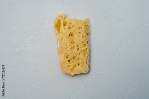 A single thin, golden roti jala rests neatly on a white plate. Its signature net-like pattern and soft texture create a simple yet appetizing traditional Malay dish that captivates the senses.