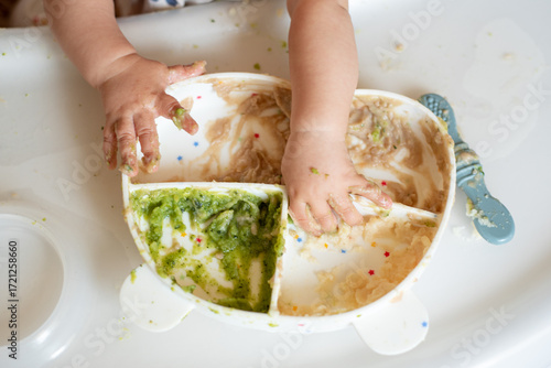 Canvas Print A small child eats porridge and vegetables at his table with his own spoon, his first complementary food