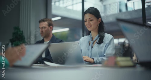 Portrait with a Female Seated Together with Office Workers Behind a Large Table, Each Working on Laptop Computers During a Team Session. Colleagues Concentrating on Corporate Tasks