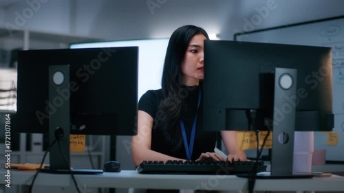 Asian Female Software Engineer Working on new innovation business startup project, Focused on Developing software, Writing code with Dual monitor screens sitting at desk in software tech office.