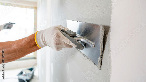 Photo of a construction workers gloved hand uses a trowel to apply plaster to a wall