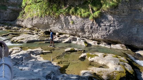 Man walks on the stones of the river while being recorded with a smartphone