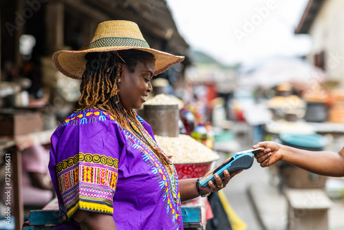 Foto Contactless transactions, small business owner, SME, local traditional African market woman accepts payment via a mobile point of sale, POS system at an outdoor market stall