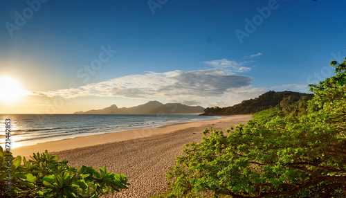 Tranquil Beach Scene Du Sunset With Lush Green Trees Overhanging Sandy Shore And Distant Mountains