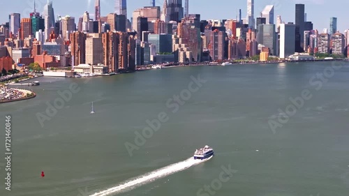 A 70mm, slow-rising pan aerial shot of a Ferry boat, ending with a helicopter, cruising along the East River, gradually revealing the Manhattan skyline and its towering architecture, in New York City.