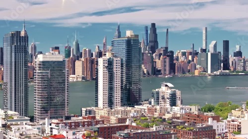 A 70mm, reversing rotational aerial shot of luxury high-rise apartments on the Brooklyn side along the East River, with the Manhattan skyline and the Empire State Building dominating the background.
