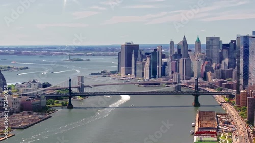 A high-flying, rotating 70mm Aerial shot over the East River of the Williamsburg bridge, the Brooklyn Bridge, and Governors Island in the distance, in-between Manhattan and Brooklyn, in New York City.