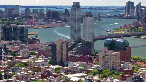A 70mm Aerial shot over the Brooklyn side of the East River of the Williamsburg bridge, slowly tracking forward with the Brooklyn Bridge and Governors Island in the background, in New York City.