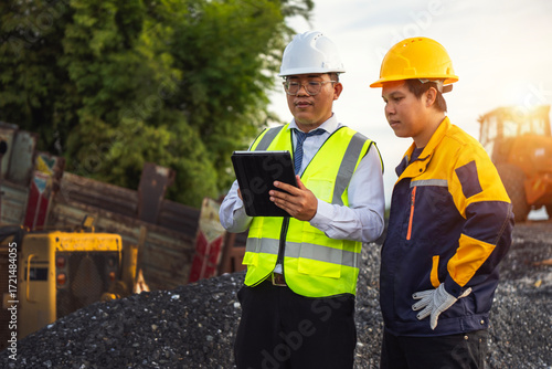 Construction Team on Site: Two construction workers, dressed in safety vests and helmets, reviewing construction plans, demonstrating expertise and collaboration in a dynamic work environment.