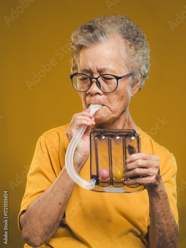 Elderly woman using incentive spirometer for lung exercise.