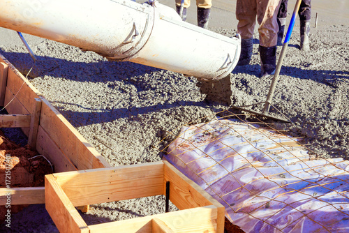 Quadro su tela Construction workers pour wet cement from chute into wooden formwork at building site cement is being poured over rebar grid that provides structural reinforcement for concrete foundation