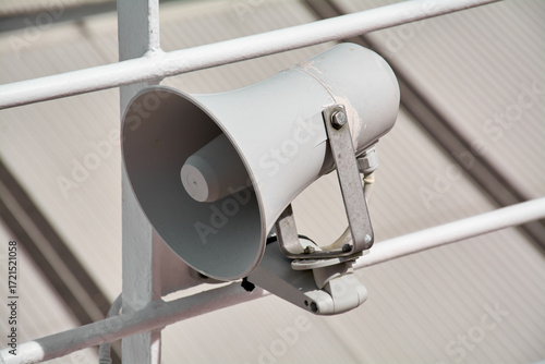 Close up of a passenger safety megaphone mounted on a white cruise ship railing. The equipment is crucial for announcing alerts and important messages.