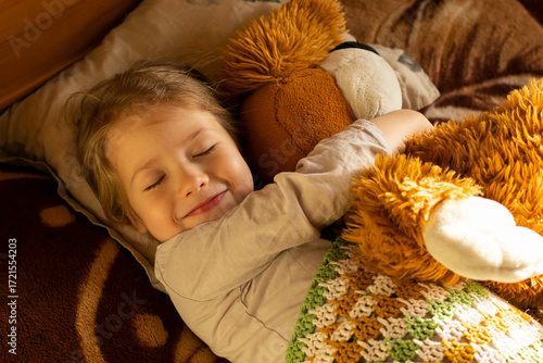 Obraz na plátne smiling little girl with closed eyes hugging her toy lying on the bed