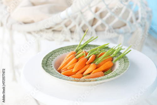 Young peeled raw carrots in a green plate on the summer porch. Selective focus.
