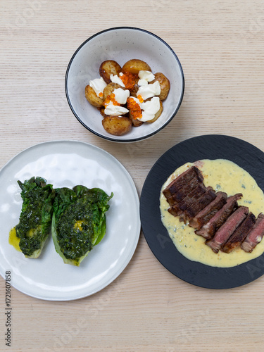 A meal of steak with sauce, roast potato, and lettuce.