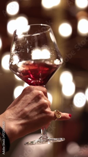Hand holding glass of red wine with bokeh lights