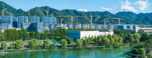 New real estate development and residential housing construction site with tower cranes by a river and green mountains.